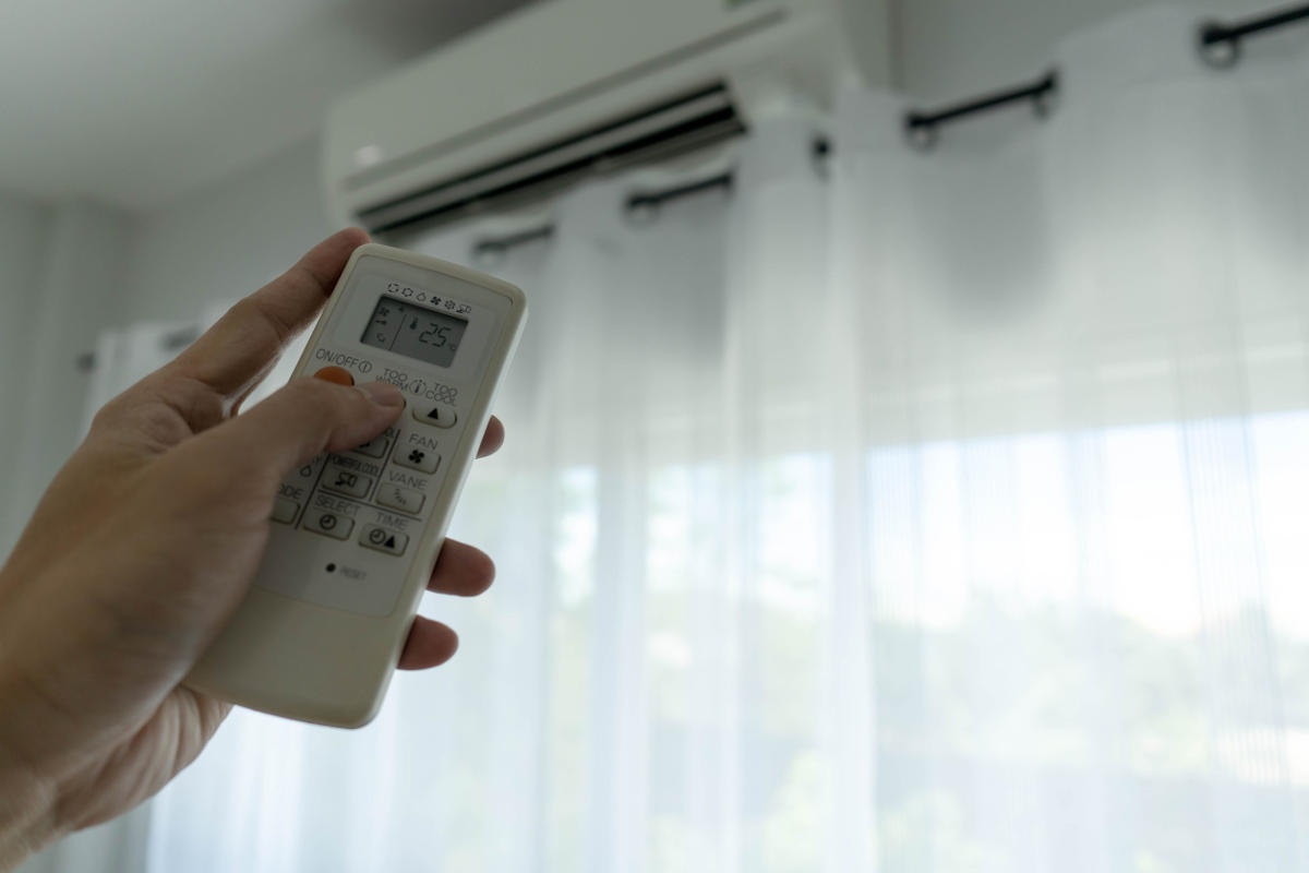 Man's hand turning off air conditioner by holding remote control