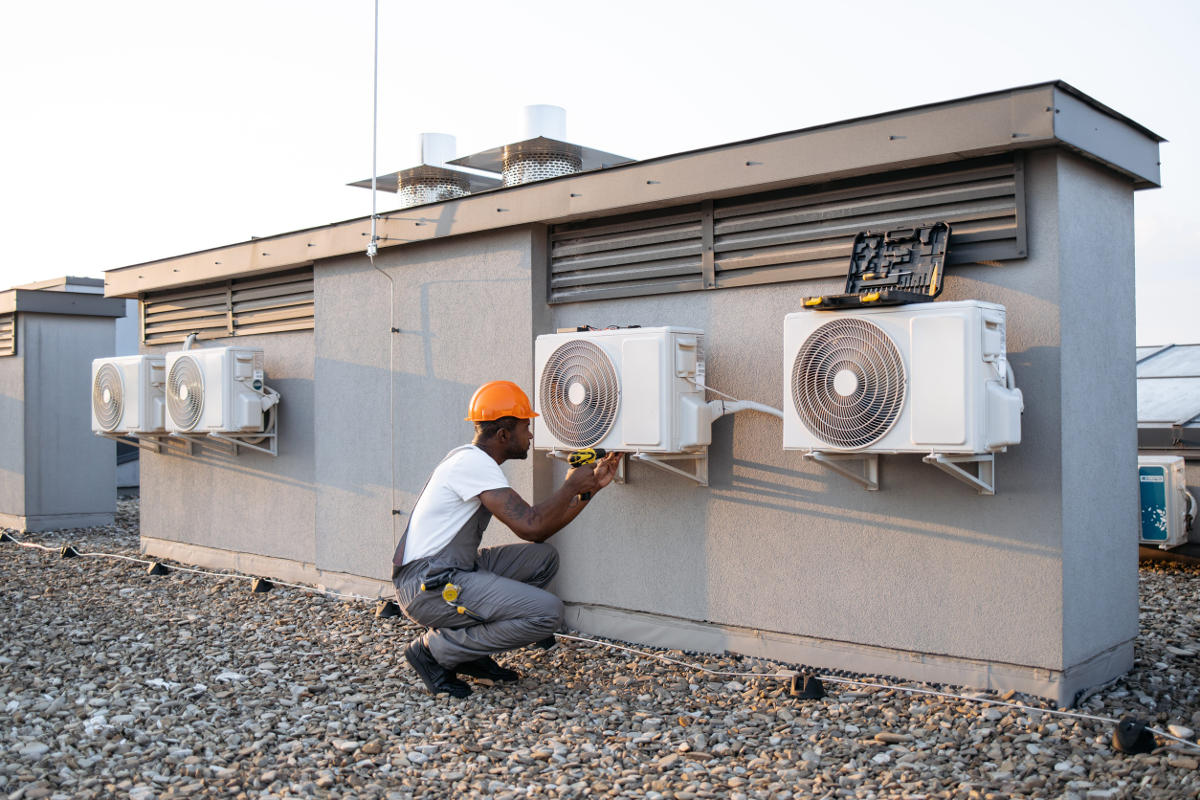 Construction worker fixing air conditioner with drill outdoors