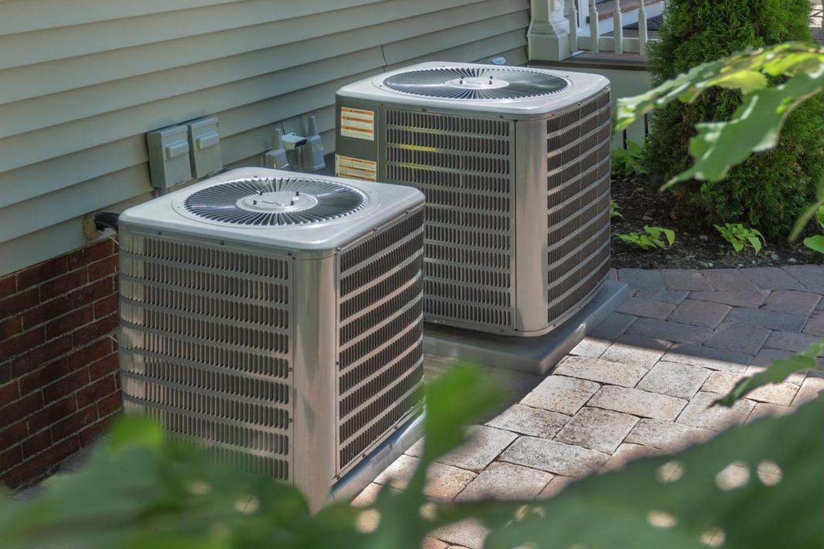 Two outdoor heat pump condenser units beside a brick house