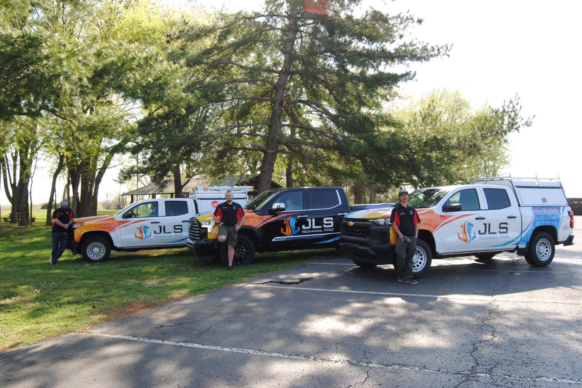Work team standing in front of 3 JLS Mechanical work trucks in company wraps