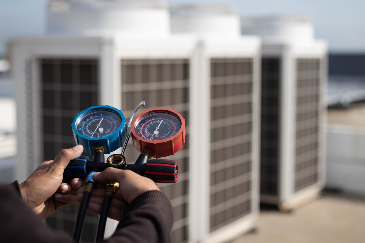 Air repair mechanic using measuring equipment for filling industrial factory air conditioners